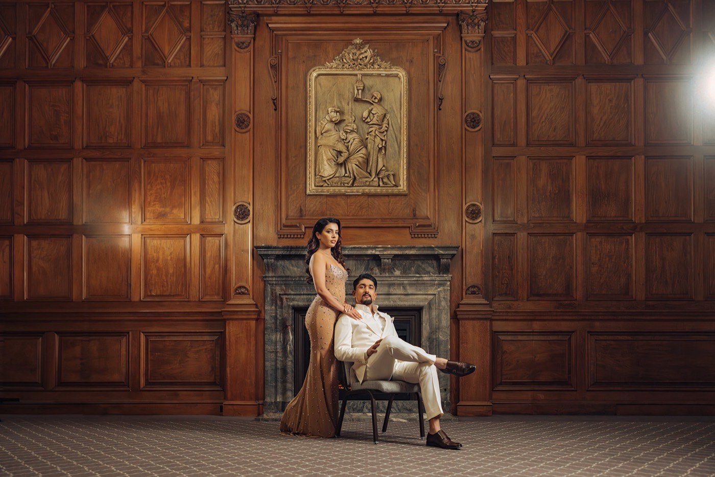 Isha and Shiv anniversary session — the couple in formalwear by a marble fireplace in the wood-panelled hall of One King West Hotel, Toronto