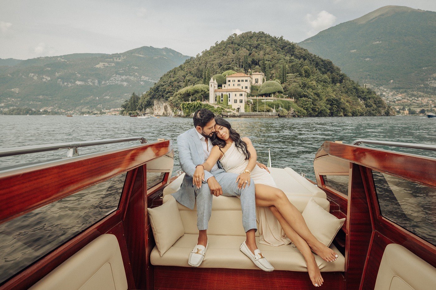 Sejal and Kbhi engagement — the couple on a classic wooden boat on Lake Como, Italy, with Villa del Balbianello behind them