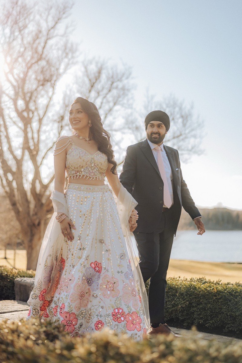 A Sikh couple in wedding attire holding hands on the lakeside grounds of the Royal Ambassador Event Centre in Caledon